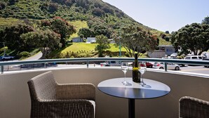 A balcony with wicker chairs and a table, overlooking a road and a hilly landscape. - Spacious Large Modern Apartment in Fantastic Location (Tauranga)