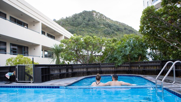 A swimming pool with a view of a mountain and a building with multiple balconies. - Spacious Large Modern Apartment in Fantastic Location (Tauranga)