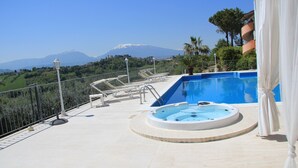 Un espace piscine doté d’un jacuzzi, de chaises longues et offrant une vue sur une montagne.