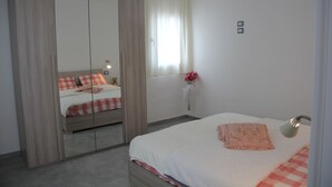 Ein Schlafzimmer mit Bett, Spiegel, Fenster mit Vorhängen und Nachttisch mit Lampe.