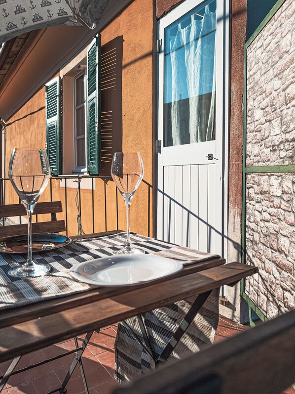 Un'area pranzo all'aperto con un tavolo apparecchiato per due persone, con un bicchiere di vino e un piatto.