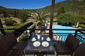 A terrace with a table set for two, overlooking a swimming pool and lush greenery. - Pegasus apartments (Skopelos)