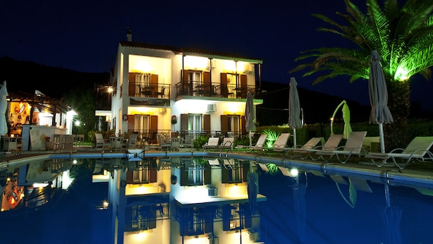 A two-story hotel with a swimming pool, lounge chairs, and umbrellas.