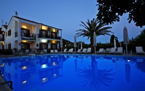 A poolside area with lounge chairs, a swimming pool, and a building with balconies. - Pegasus apartments (Skopelos)