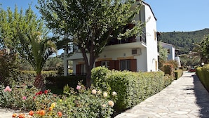 A two-story building with a stone pathway leading to a white facade with brown shutters.