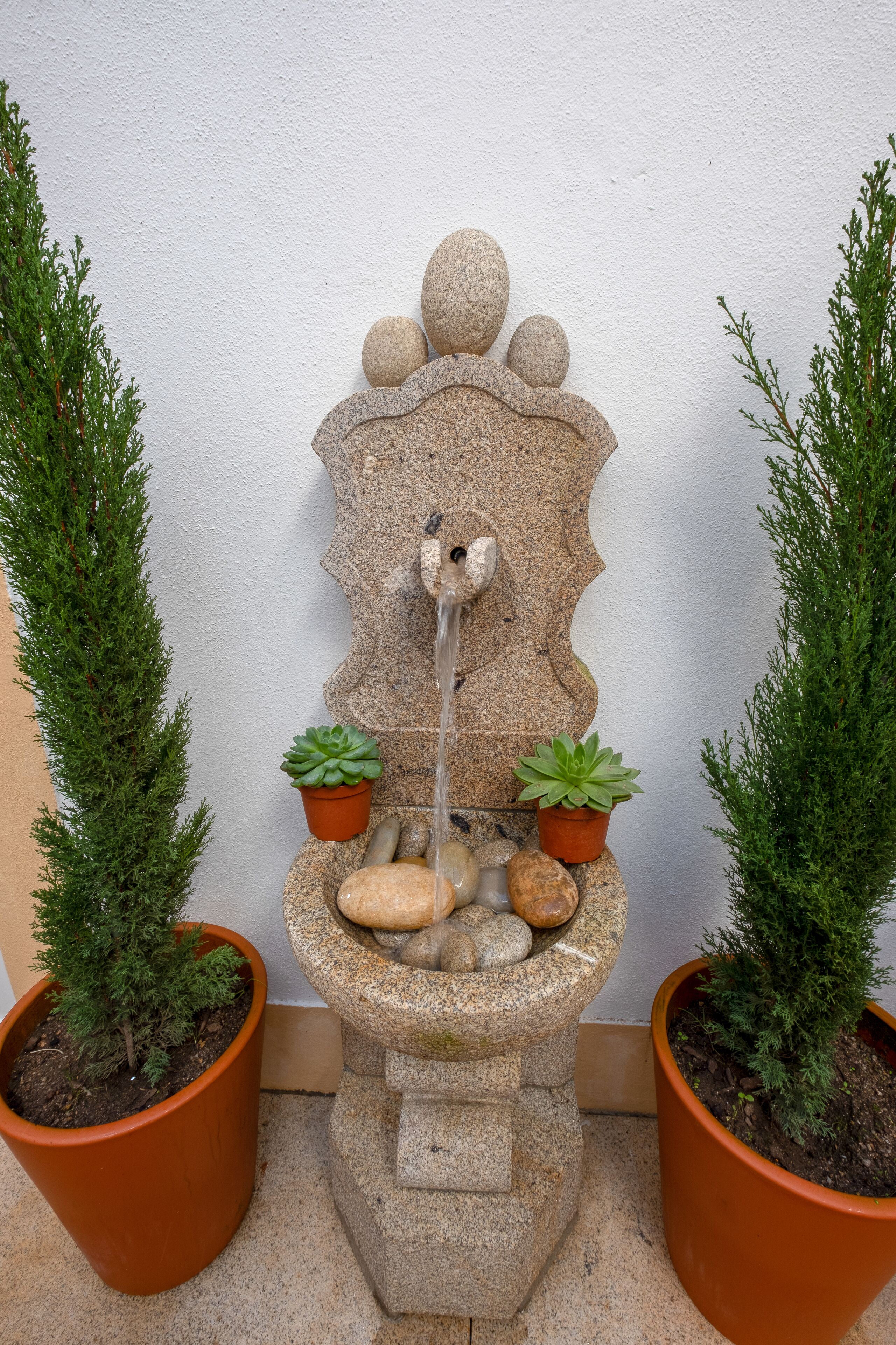 Una fontana in pietra con un elemento d'acqua a cascata, circondata da piante in vaso.