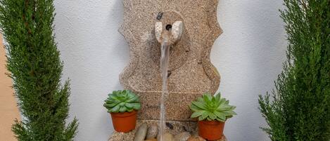 A stone fountain with a cascading water feature, surrounded by potted plants.