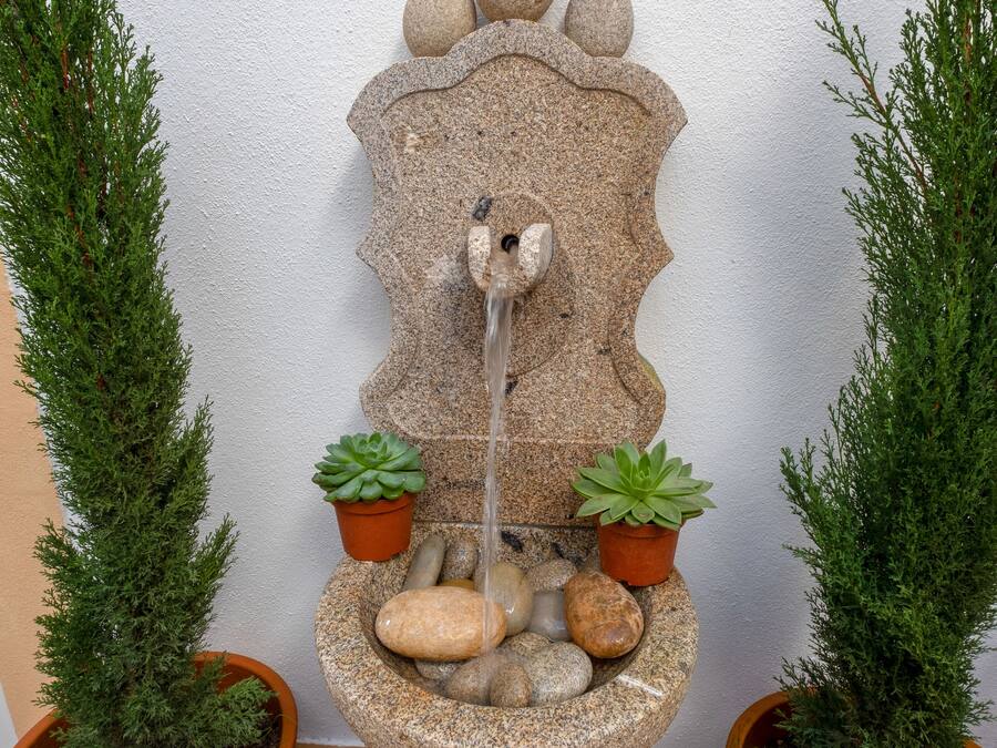 Una fontana in pietra con un elemento d'acqua a cascata, circondata da piante in vaso.