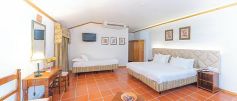 A hotel room with a bed, a sofa, a desk with a lamp, a small table with a bowl, and a TV on the wall.