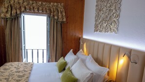 Een hotelkamer met een bed, gordijnen, een decoratief wandobject en een raam met uitzicht.