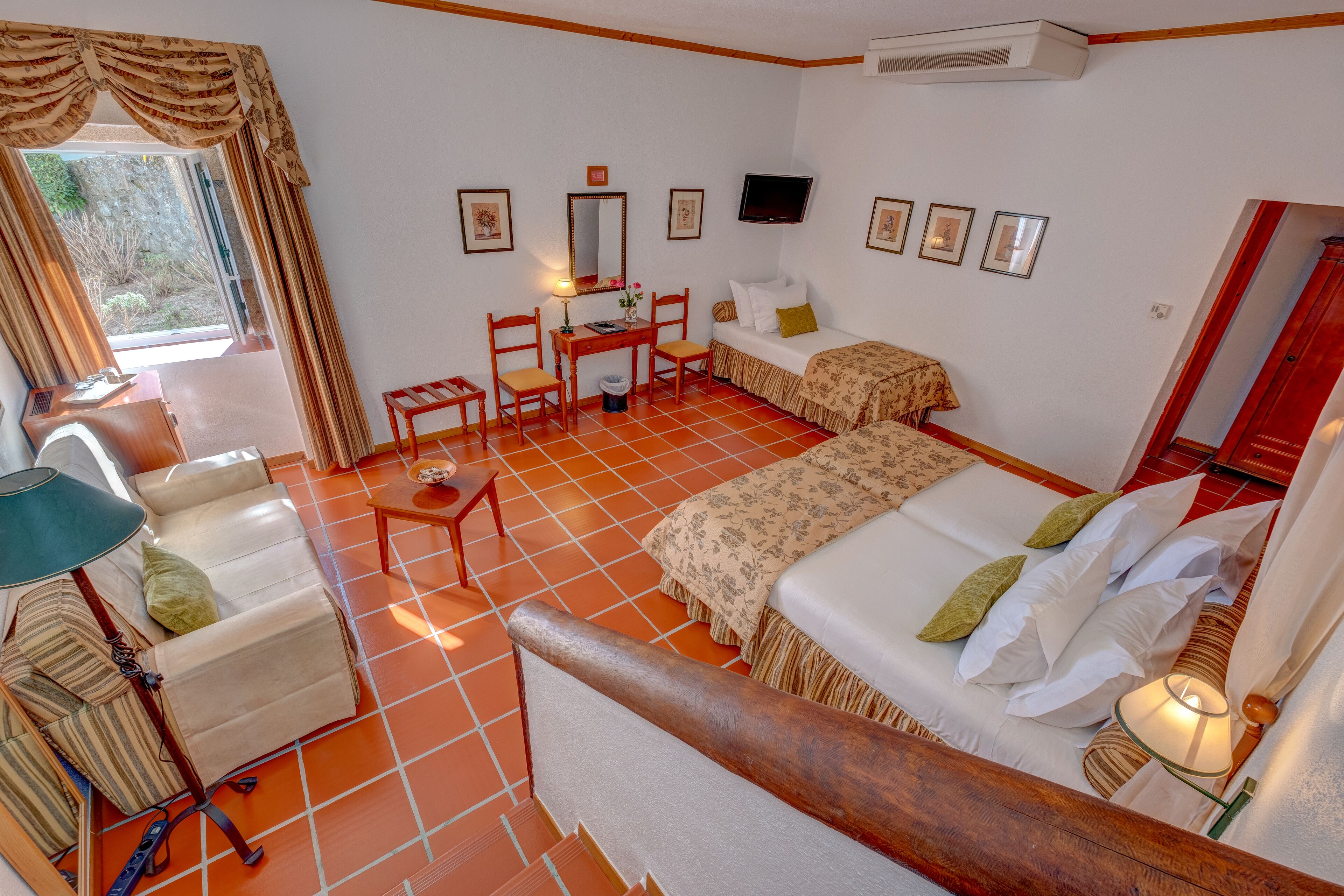 Quarto com uma cama, escrivaninha, cadeira, luminária e televisão.