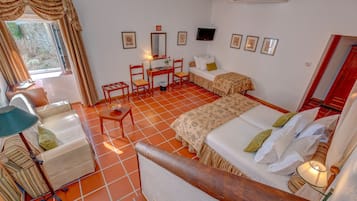 Quarto com uma cama, escrivaninha, cadeira, luminária e televisão.