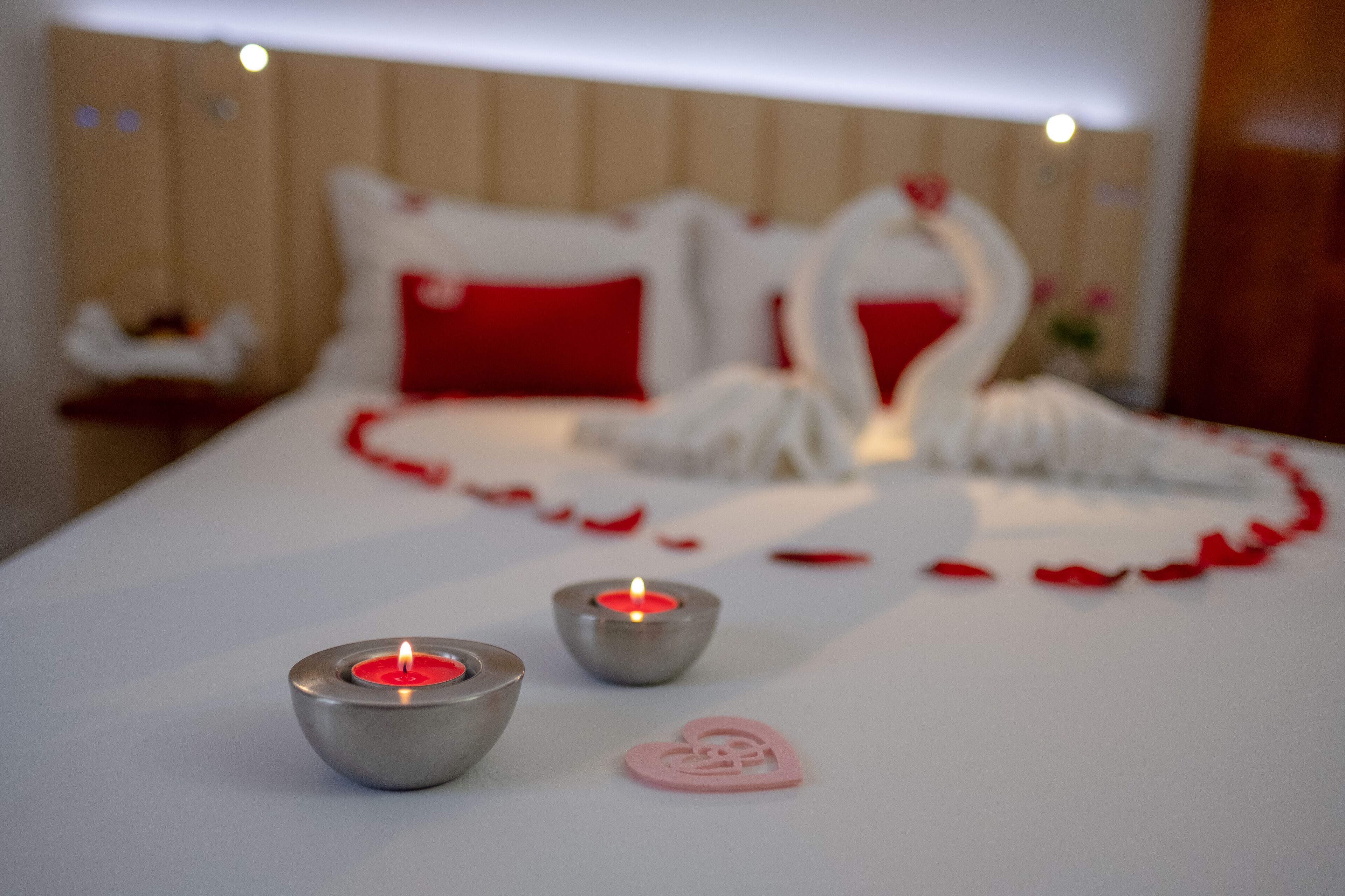 Una cama con ropa de cama roja y blanca, dos velas y una decoración con forma de corazón.
