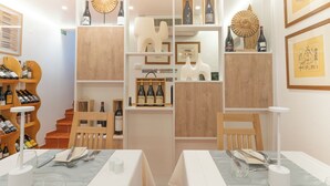 Een restaurantinterieur met houten meubels, witte tafels en planken met wijnflessen.