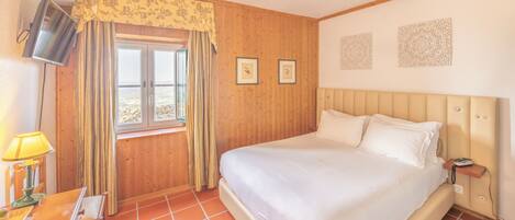 A bedroom with a large bed, wooden walls, a window with curtains, and a television on the wall.
