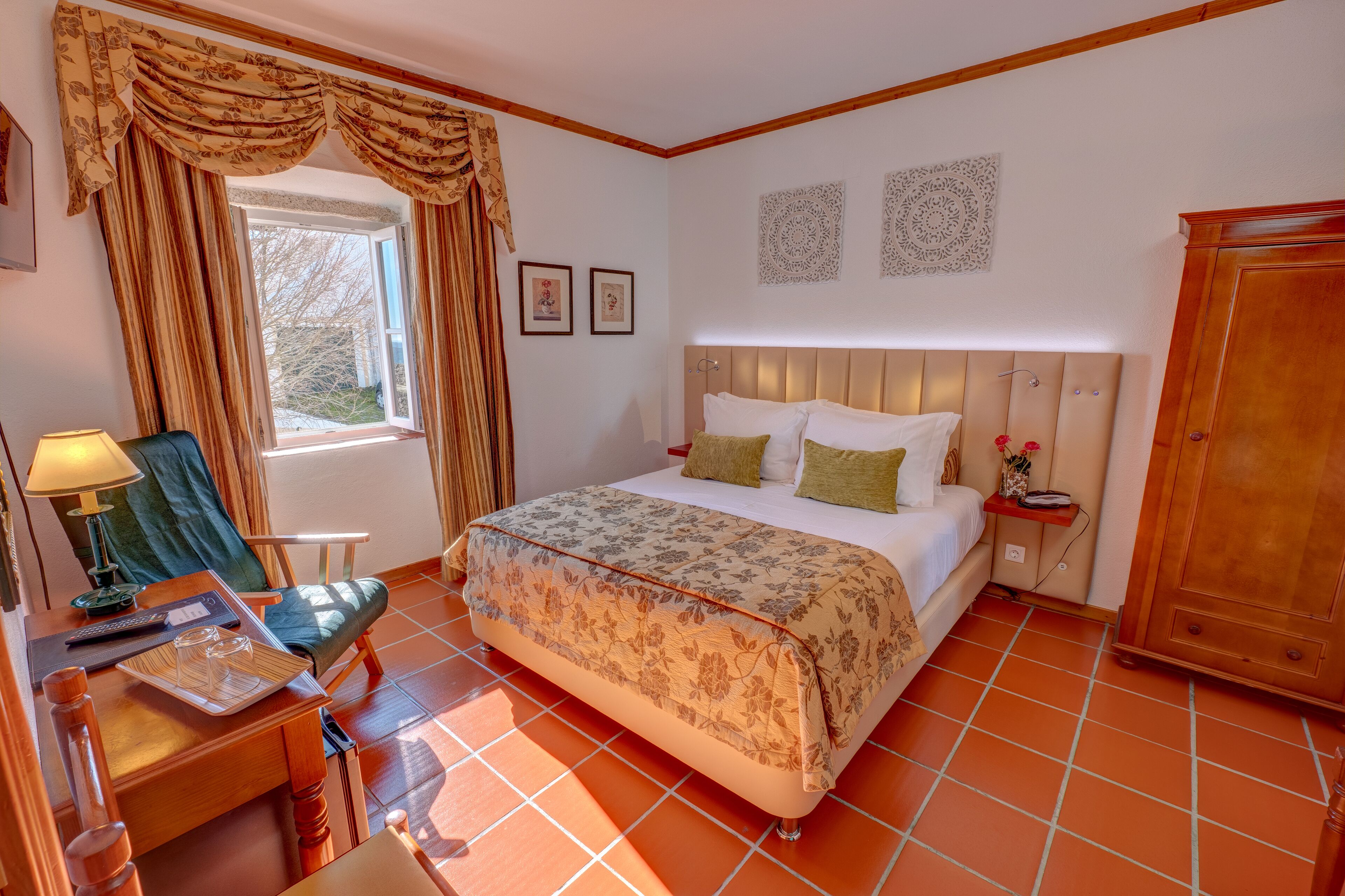 Un dormitorio con cama, escritorio con lámpara, silla, ventana con cortinas y armario.