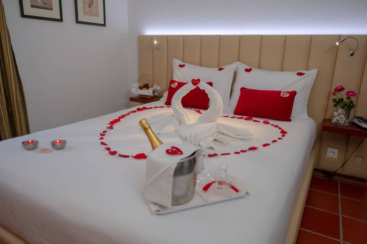 Ein ordentlich bezogenes Bett mit einer schwanenförmigen Dekoration, roten Rosenblättern und einer Champagnerflasche.