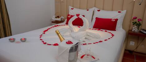 A neatly made bed with a swan-shaped centerpiece, red rose petals, and a bottle of champagne.