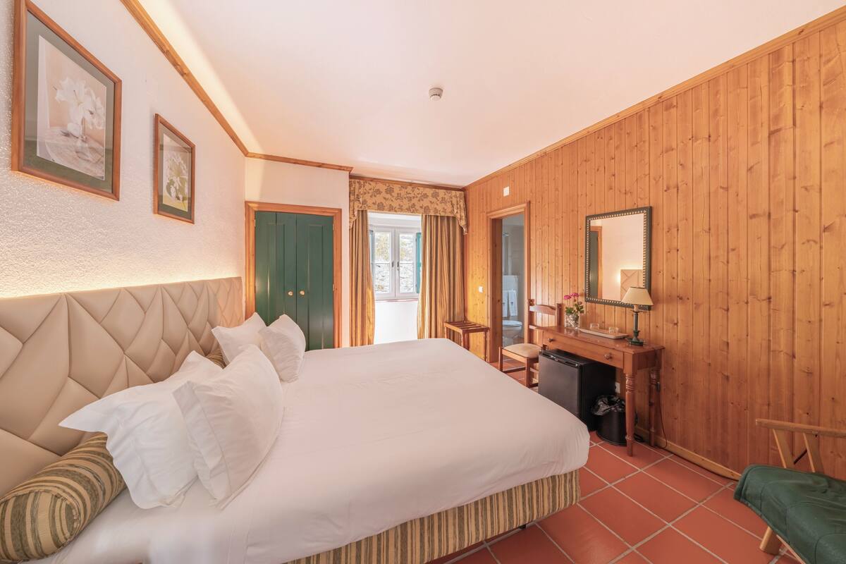 Ein Hotelzimmer mit einem großen Bett, Holzwänden, einem Schreibtisch mit Spiegel und Blick ins Freie.