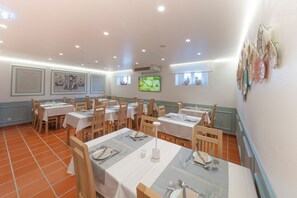 A dining area with tables set for service, a television mounted on the wall, and framed artwork on the walls. - Hotel Dom Manuel (Marvao)