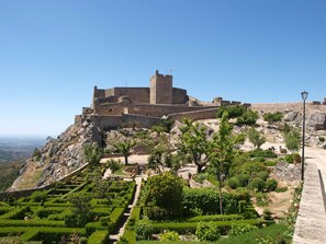 A historic stone fortress with a central tower, surrounded by terraced gardens and a clear sky. - Hotel Dom Manuel (Marvao)