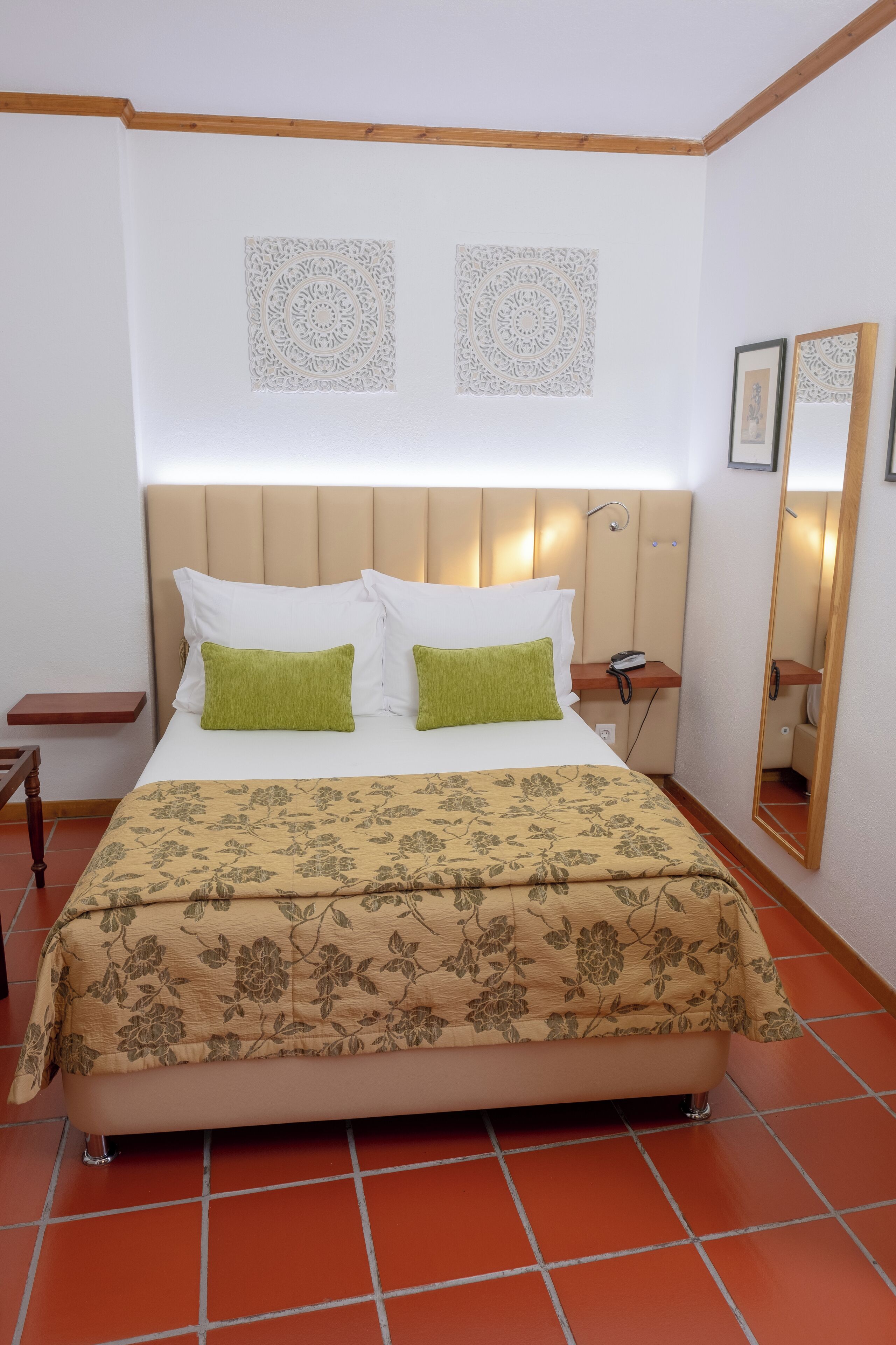A neatly made bed with a floral bedspread, a headboard with built-in lighting, and a bedside table with a phone.