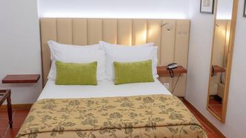 A neatly made bed with a floral bedspread, a headboard with built-in lighting, and a bedside table with a phone.