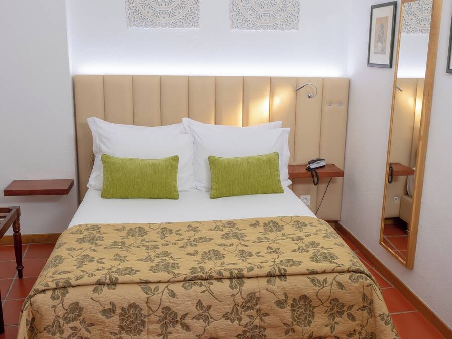 A neatly made bed with a floral bedspread, a headboard with built-in lighting, and a bedside table with a phone.