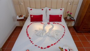 Een bed met rode kussens, een rozenblaadjesarrangement in de vorm van een hart en een handdoek gevouwen als een zwaan.