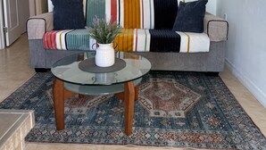 A living room with a gray sofa, colorful cushions, a glass coffee table, and a patterned rug.