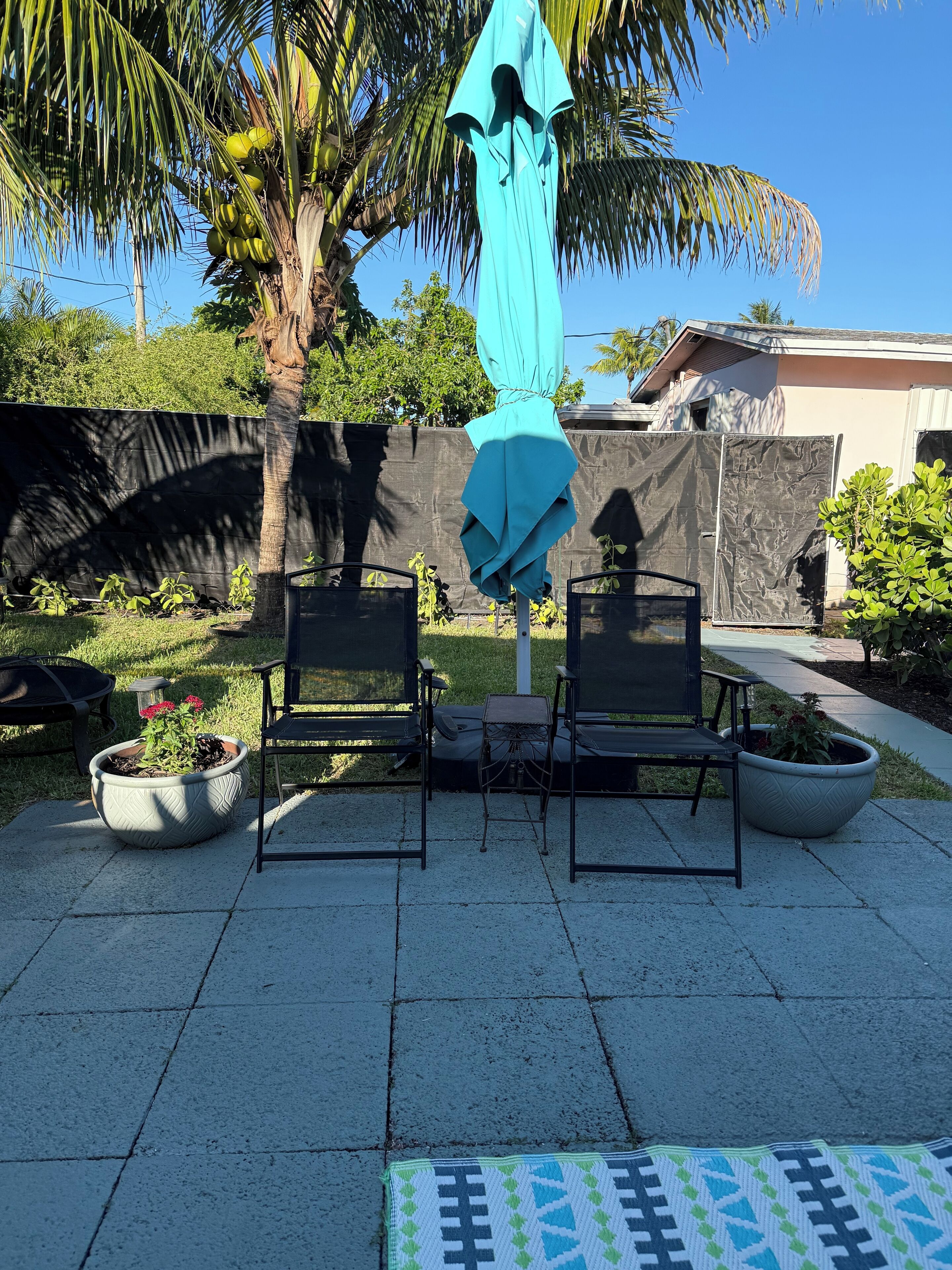 Eine Terrassenausstattung mit Sitzgelegenheit, Sonnenschirm und Pflanzkübeln.