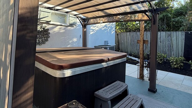 A covered outdoor hot tub area with a wooden bench and a small table.