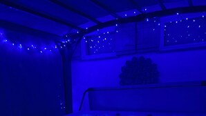 A hot tub with a wooden bench in a room with a sloped ceiling and string lights.