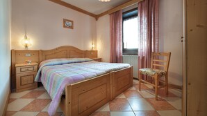 A bedroom with a wooden bed, bedside tables, a chair, and a window with curtains. - Ringemel-2 apartments (Livigno)