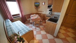 A compact living space with a sofa, dining table, chairs, a small kitchen area, and a television. - Ringemel-2 apartments (Livigno)