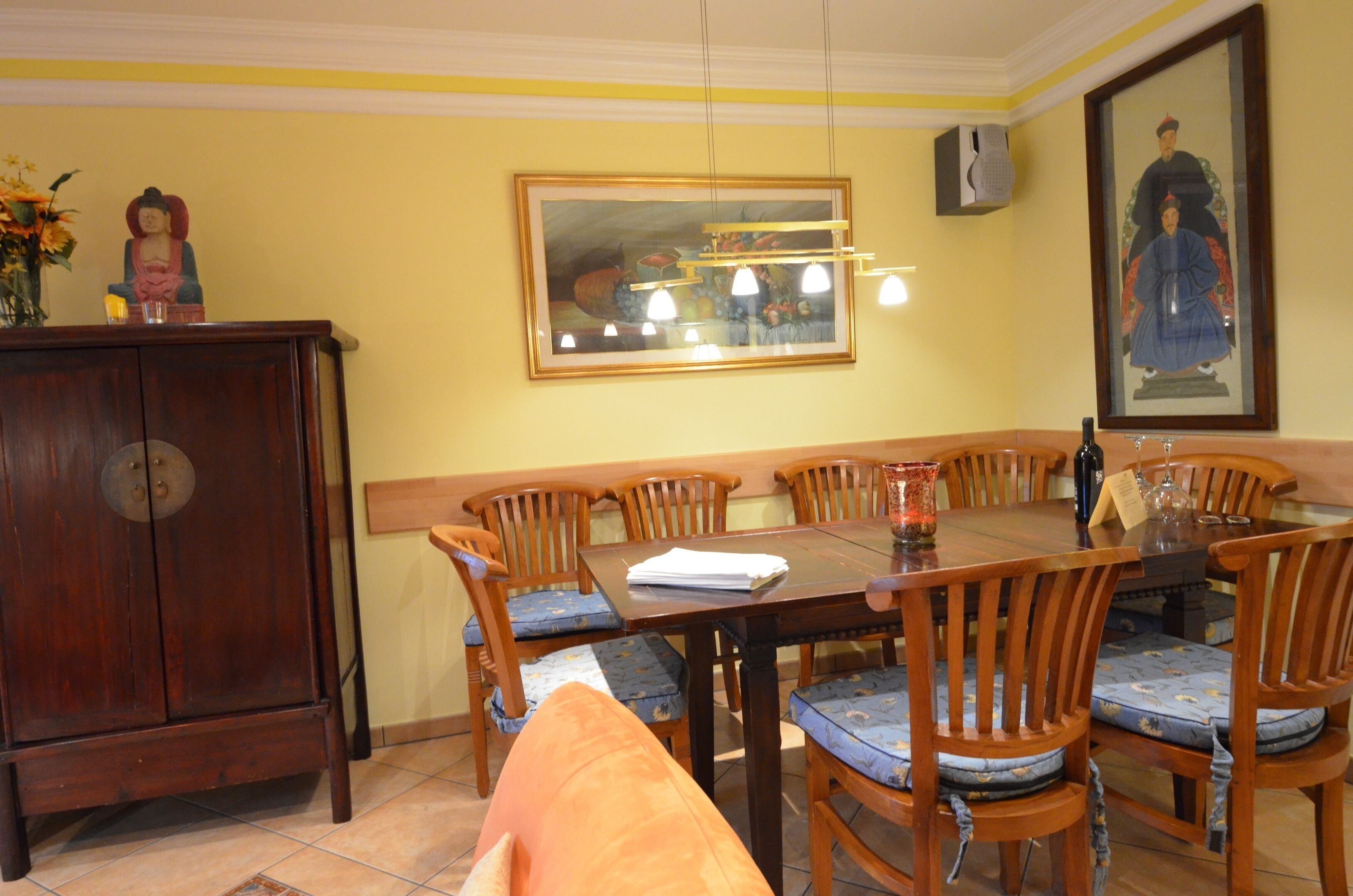 A dining area with a wooden table and chairs, a cabinet, and a framed painting on the wall.