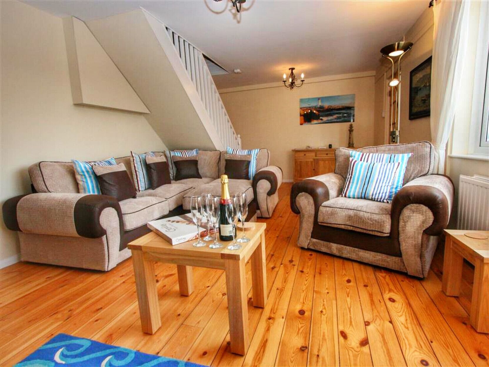 Ein gemütliches Wohnzimmer mit Holzboden, zwei Sofas mit gestreiften Kissen, einem Couchtisch mit Flasche und Gläsern sowie einer Treppe, die zu einer anderen Ebene führt.