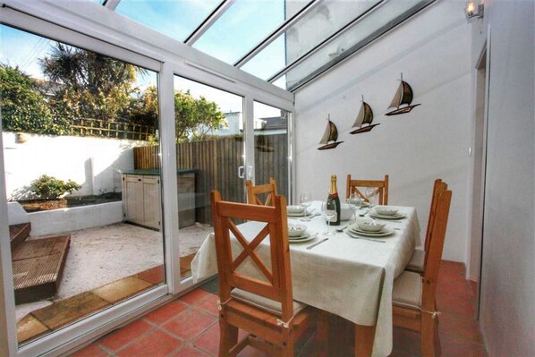 A dining area with a glass door leading to a patio, a table set for two, and sailboat decorations on the wall.