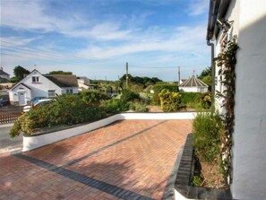 A paved driveway leading to a white house with a garden.