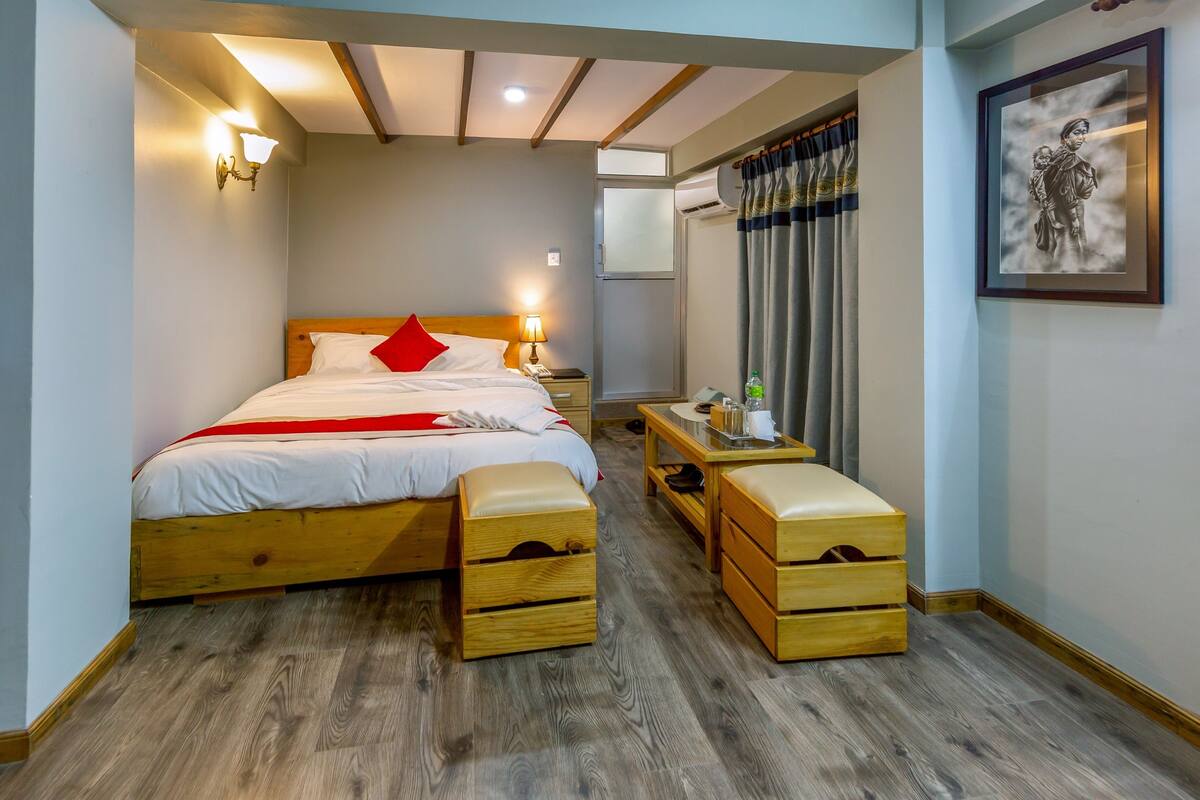A bedroom with a wooden bed, bedside tables, a bench, and a wall-mounted air conditioner.