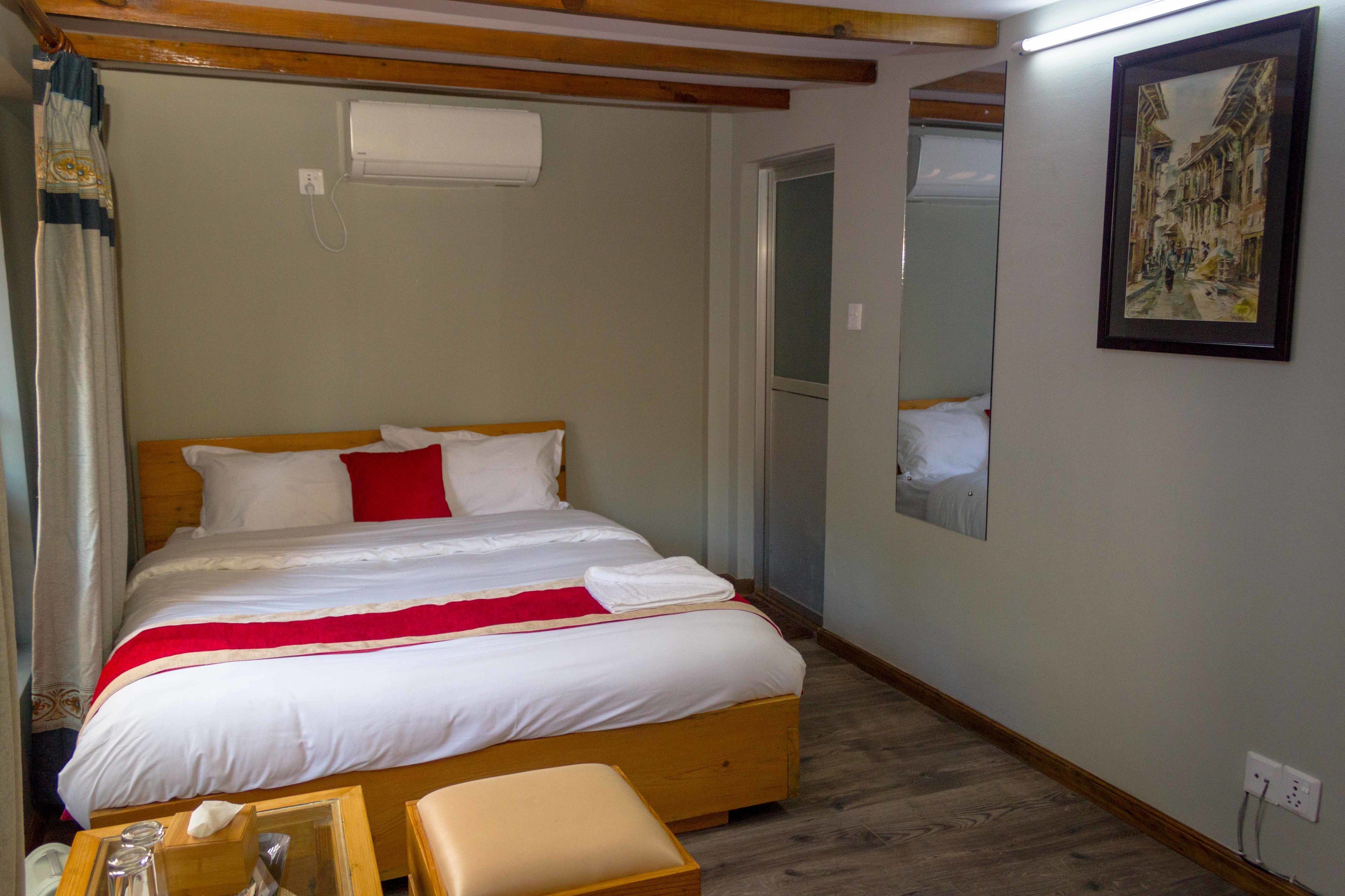 A neatly made bed with white and red bedding, a wooden headboard, and a bedside table with a lamp.