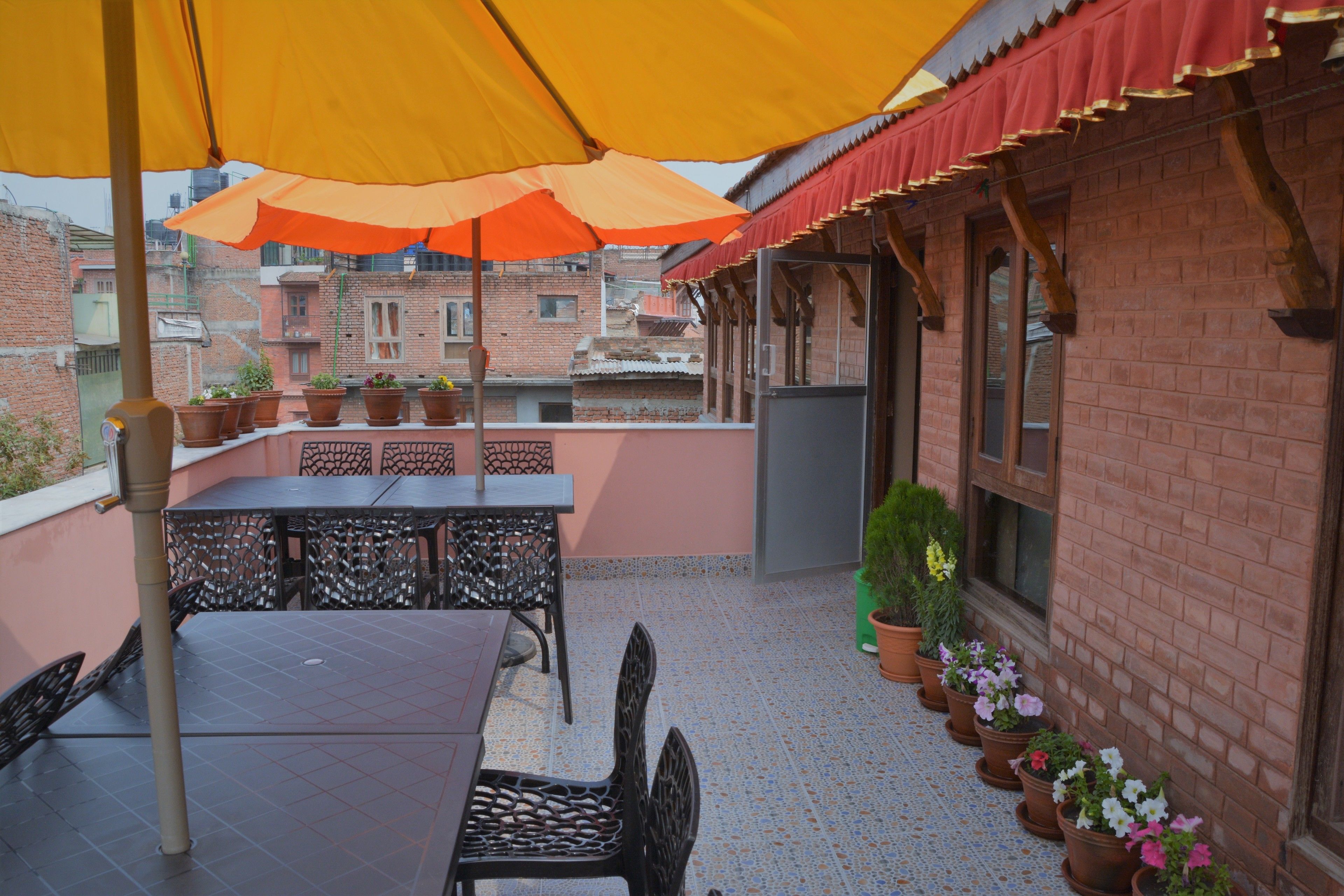 A terrace with a table and chairs, potted plants, and a red awning.