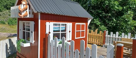 A small red wooden building with a white picket fence, a metal roof, and a window with white shutters.