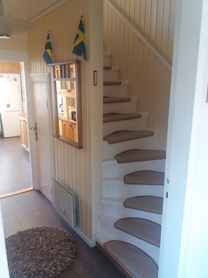 Una escalera con detalles de madera y una puerta blanca con un ventanal pequeño.