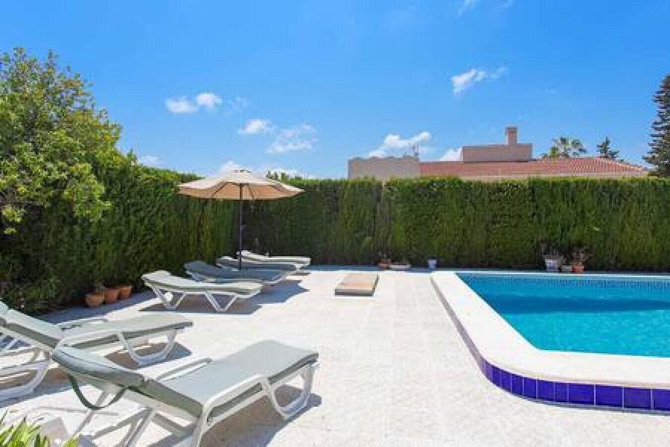 Ein Swimmingpool mit Liegestühlen und einem Sonnenschirm, umgeben von viel Grün.