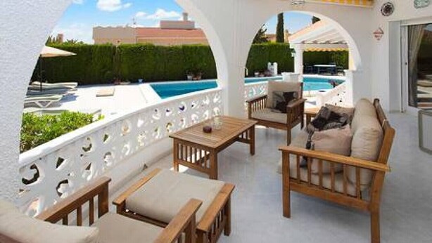 An outdoor patio with wooden furniture and a view of a swimming pool.