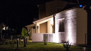 A modern house with a well-lit exterior, a covered porch, and a small lawn area.