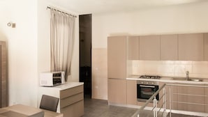 A compact kitchen with a microwave, stove, oven, and a small dining area with a chair and table.