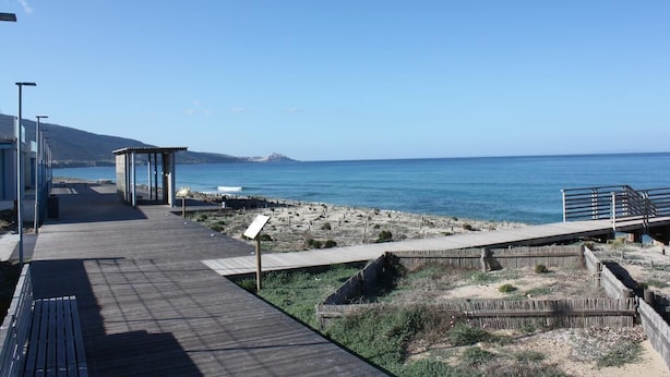 A wooden boardwalk leading to a beach with a clear view of the ocean and a distant mountain.