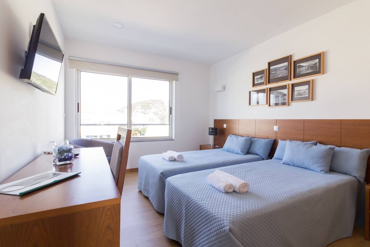 Habitación de hotel con dos camas, un escritorio, un televisor y una ventana con vistas.